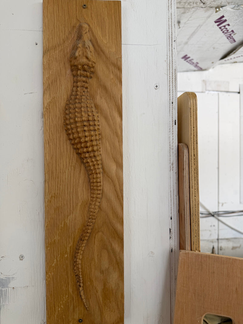 A carved wooden alligator wall hanging mounted on a white wall, showing detailed wood grain and texture.