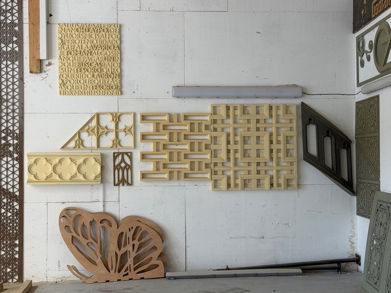 A collection of decorative architectural panels and screens displayed against a white wall, including a butterfly-shaped screen, geometric lattice panels, and carved wooden pieces in light and medium brown tones.